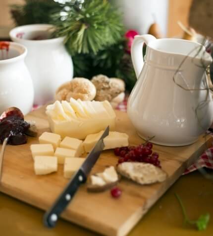 Tagliere di legno con assortimento di formaggi, ribes rossi e un coltello, in un'atmosfera festiva natalizia.