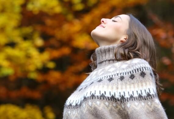 Donna con maglione grigio, occhi chiusi, sfondo autunnale sfocato.