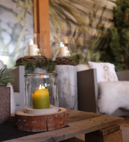 Una stanza accogliente con un tavolo in legno, una candela gialla, una pianta e un grande murale di piante sullo sfondo.