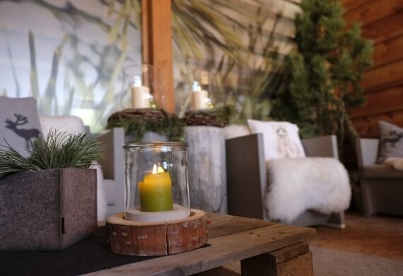 Una stanza accogliente con panchina in legno, candele, piante e grandi finestre che mostrano erba pampas e cielo blu.