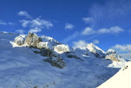 Paesaggio invernale sereno con montagne innevate sotto un cielo blu brillante e una collina coperta di neve in primo piano.