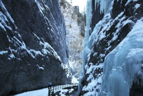Scena invernale serena con una valle innevata, pareti rocciose e una cascata ghiacciata, che trasmette tranquillità.