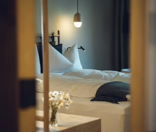 Camera d'hotel con letto bianco, fiori bianchi e lampadario.