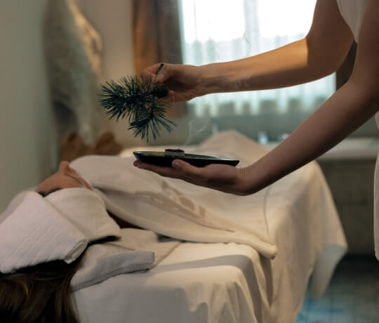 Persona su un tavolo da massaggio con fumi e aghi di pino.