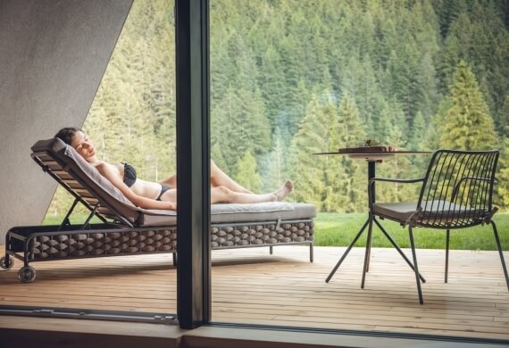 Donna su chaise lounge in legno, circondata da pini.