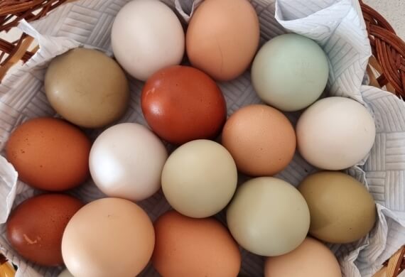 Uova colorate disposte in un cesto di vimini foderato di carta bianca, creando un'atmosfera elegante e naturale.