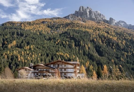 Hotel at mountain base, surrounded by green trees and blue sky. Hotel alla base della montagna, circondato da alberi verdi e cielo blu.