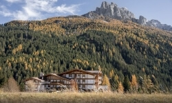 Edificio a più piani con tetto inclinato davanti a una montagna alberata.
