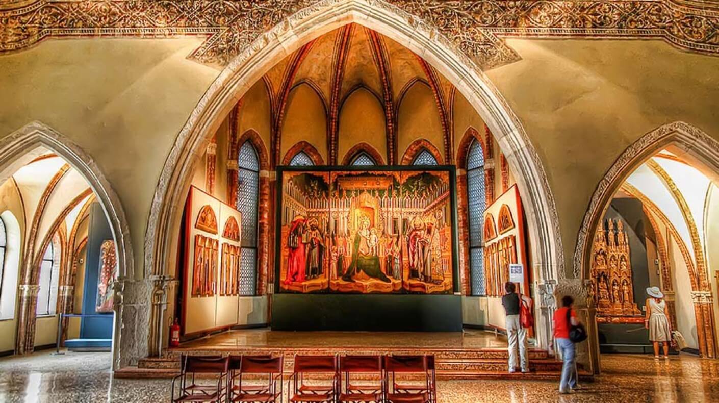 Una grande stanza ornata con soffitti a volta, dipinti, persone in contemplazione e un'atmosfera di reverenza.