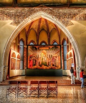 Una stanza gotica ornata con un dipinto allegorico, pavimento in marmo rosa e due visitatori che osservano un segno.