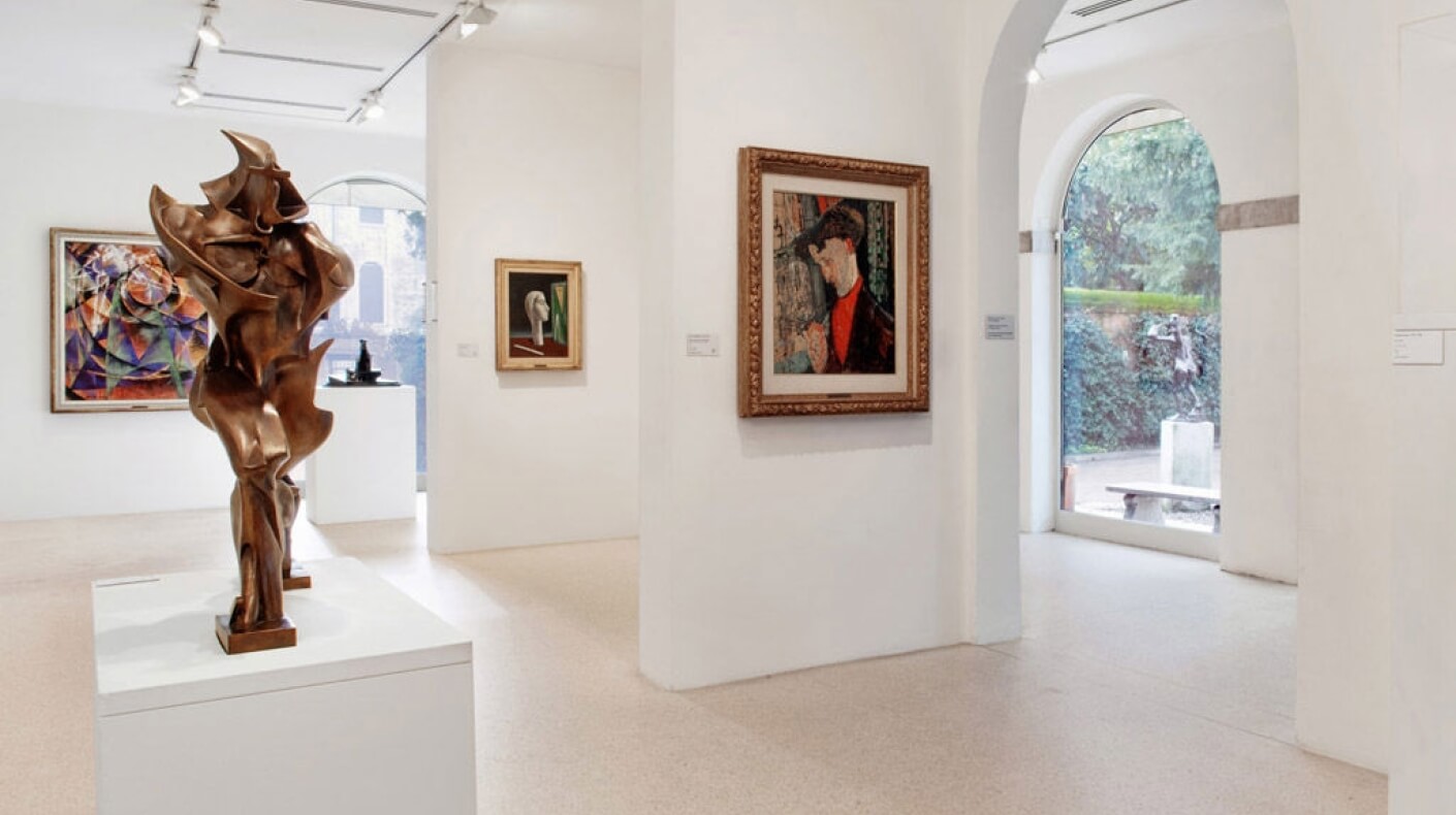 Una sala d'arte con sculture e dipinti, un'opera astratta in bronzo su un piedistallo bianco in primo piano.