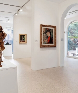 Museo con pareti bianche, scultura bronzea in primo piano e porte ad arco che mostrano alberi all'esterno. Atmosfera tranquilla.