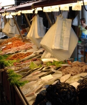 Un mercato del pesce affollato con una varietà di frutti di mare freschi, illuminato da luci calde e con clienti attivi.