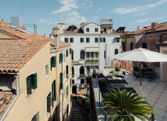 Vista serena di Venezia con edifici bianchi e gialli, canale, gondole, Hotel Lombina e palme sotto un cielo blu.