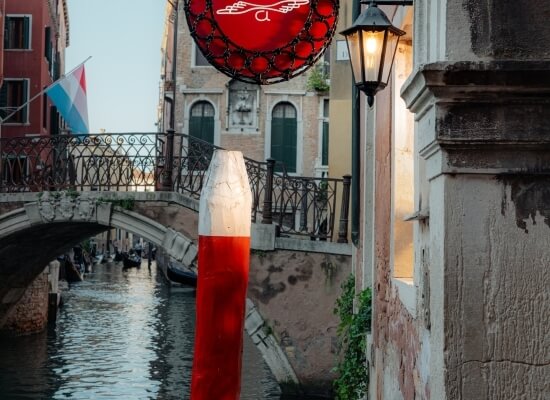 Canale sereno a Venezia con ponte, edifici, lanternina nera e riflessi sull'acqua, trasmette un'atmosfera di tranquillità.