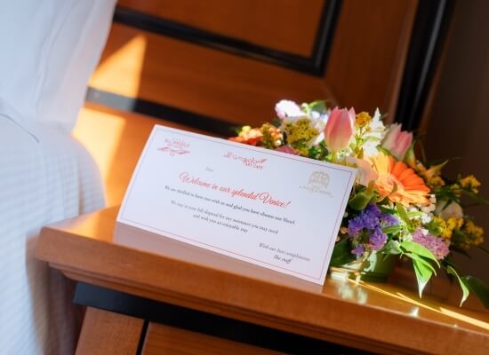 Welcome card with red text and a bouquet of colorful flowers on a light wooden table, creating an inviting hotel atmosphere.