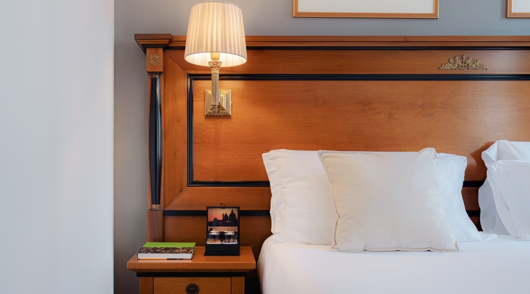 Camera d'hotel con letto, testiera in legno e lampada a muro.