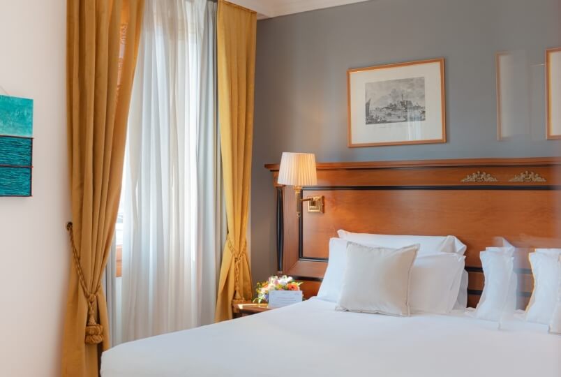 Camera da letto serena con letto centrale, lenzuola bianche, testiera in legno, lampade e pareti grigie.