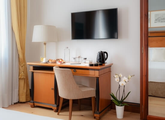 Camera d'hotel con scrivania, sedia, TV a schermo piatto, pianta di orchidea e letto con testiera marrone.