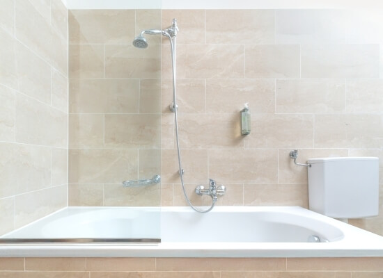 Bagno sereno con vasca bianca, rubinetto in argento, dispenser di sapone e pareti in piastrelle beige.