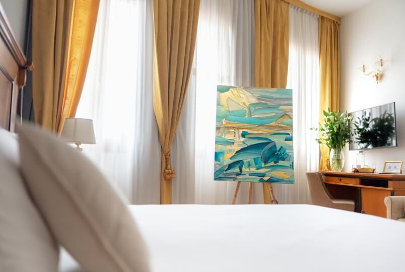 Camera elegante con letto bianco, pittura astratta, tende gialle, scrivania in legno e area salotto accogliente.