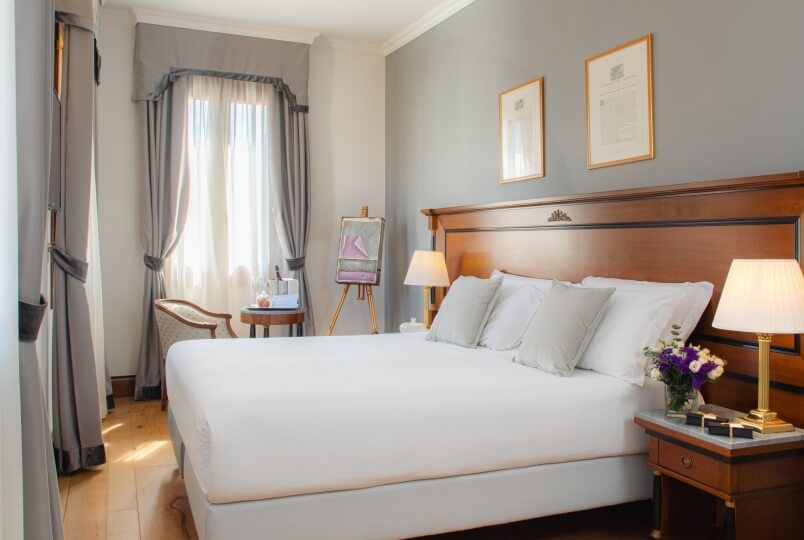 Camera da letto serena con letto grande, luce naturale, decorazioni eleganti e un tavolo con vino e un dipinto di scarpa.