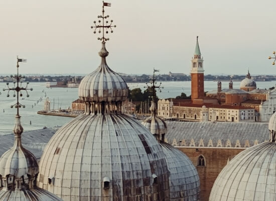 Vista di Venezia con una chiesa dai tre grandi cupole e skyline della città sullo sfondo, bandiere e decorazioni visibili.