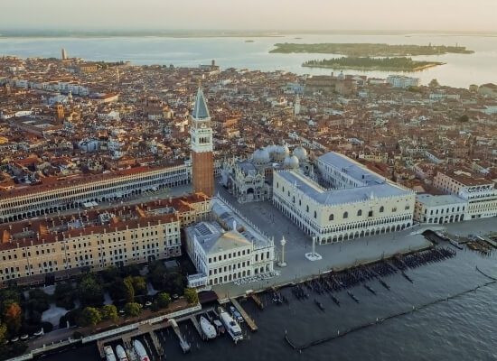 Vista aerea di Venezia al tramonto, con Piazza San Marco, Campanile, Basilica e Palazzo Ducale, circondati da canali.