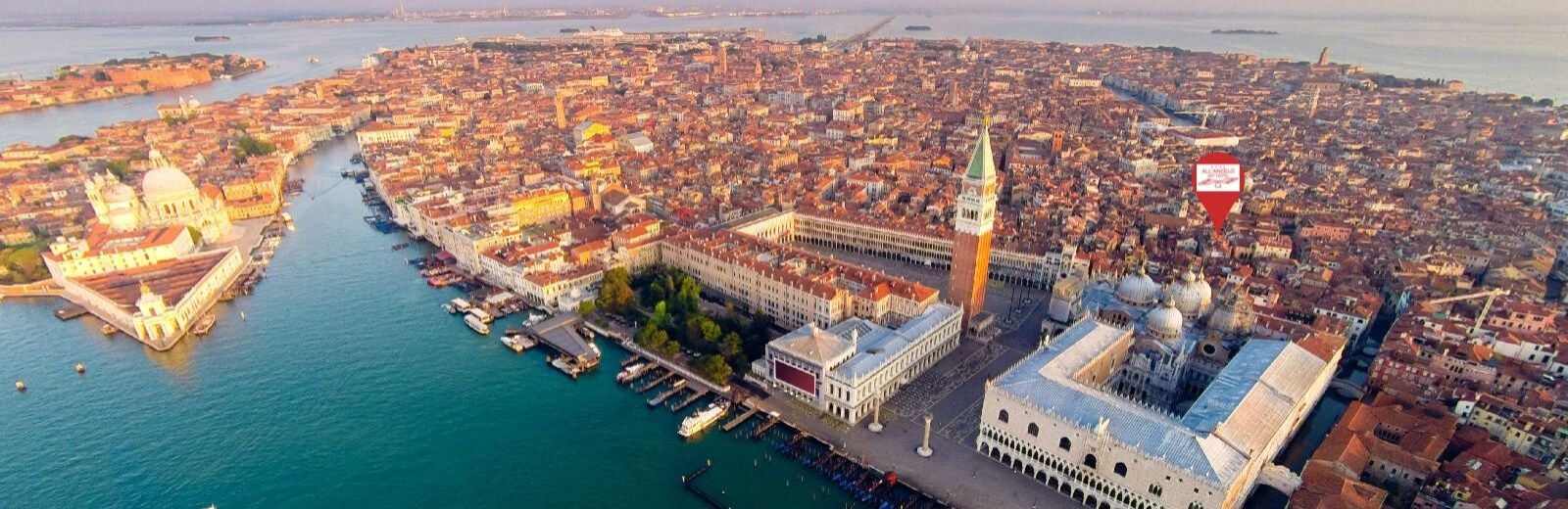 Vista aerea di Venezia con edifici arancioni, canali, un edificio bianco con cupola e un grande edificio con torre.
