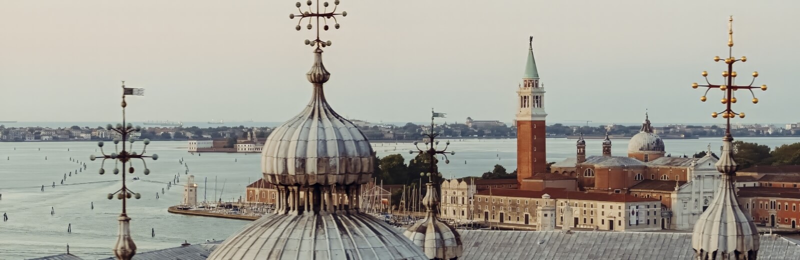 Vista aerea di una città con un grande dome, un campanile e edifici con tetti rossi, affacciati su un corpo d'acqua.