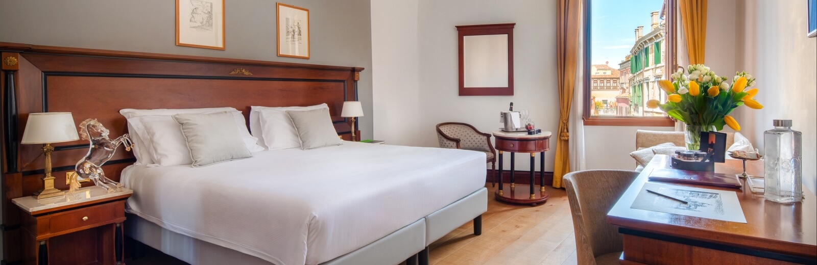 Camera d'albergo lussuosa con letto grande, scrivania, finestra sulla città e decorazioni classiche in legno scuro.