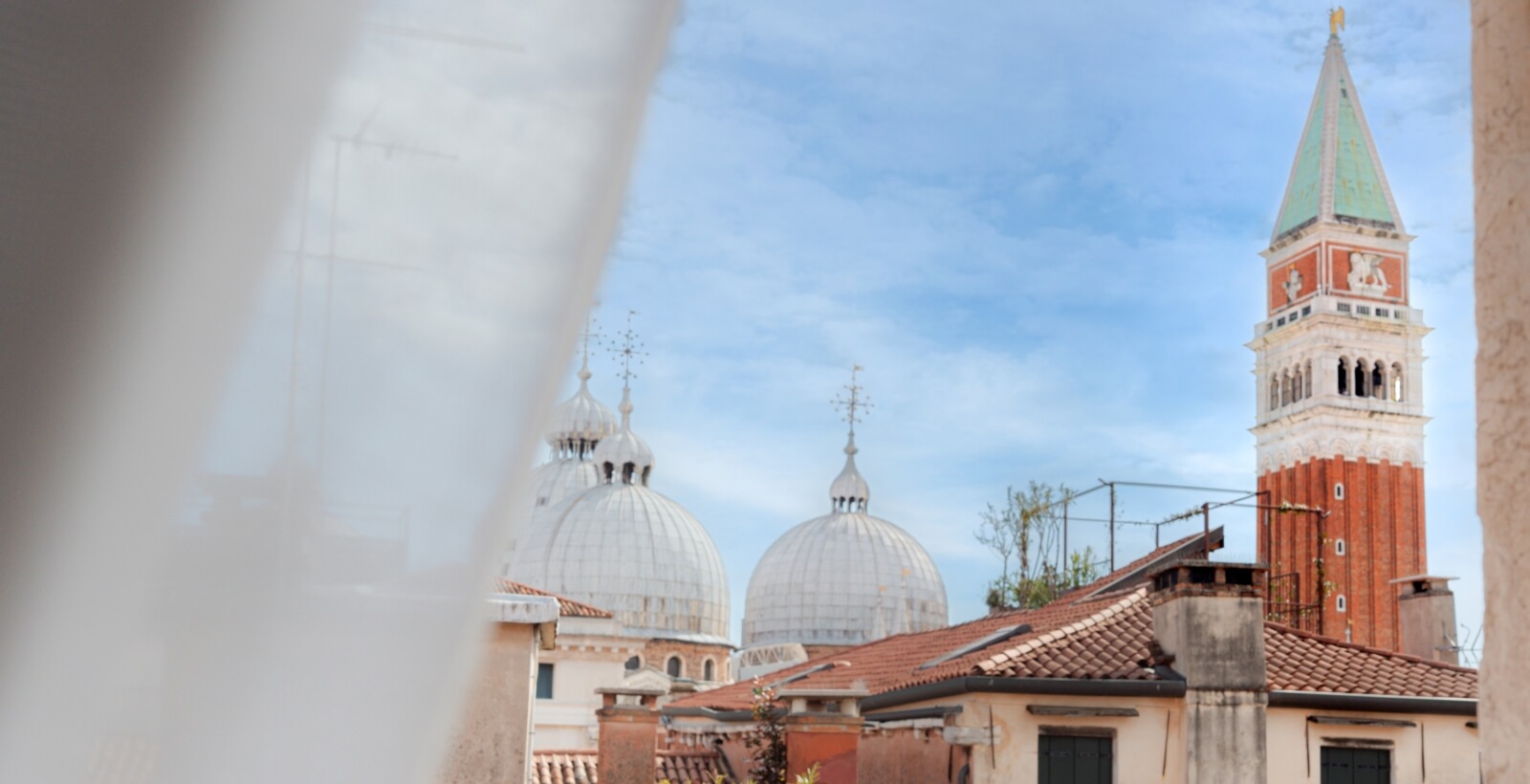 Vista di Venezia con il Campanile di San Marco, due cupole bianche e un cielo blu sereno.