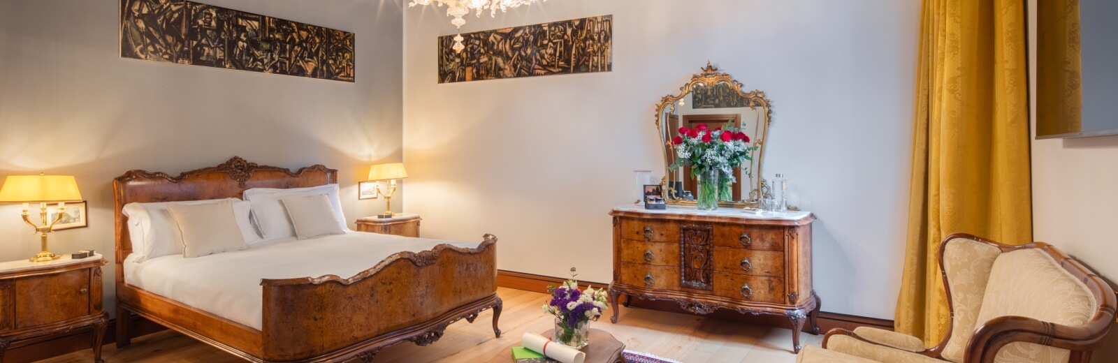 Camera da letto tradizionale con letto grande, comò, sedia, pareti bianche e mobili in legno scuro, atmosfera accogliente.