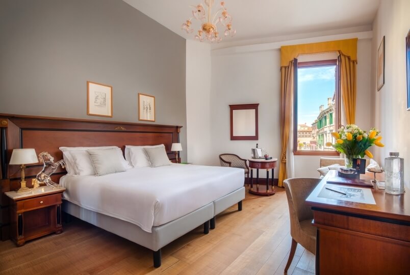 Camera d'hotel accogliente con letto, scrivania, finestre con tende gialle e lampade sui comodini. Atmosfera invitante.