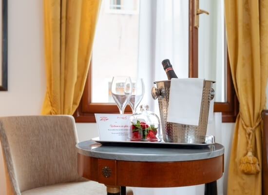 Tavolo rotondo in legno con champagne, flute, e decorazioni floreali, allestito per un'occasione romantica.