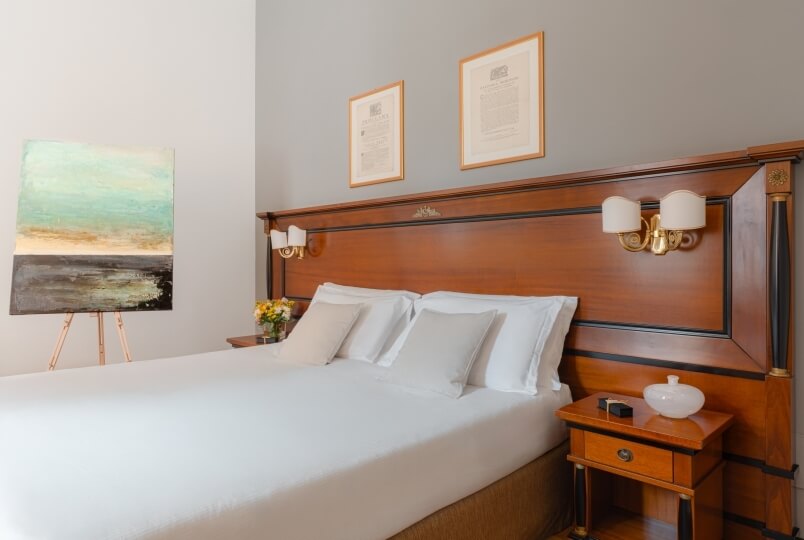 Camera da letto serena con letto bianco, comodino, opere d'arte e tonalità di grigio, marrone e bianco.