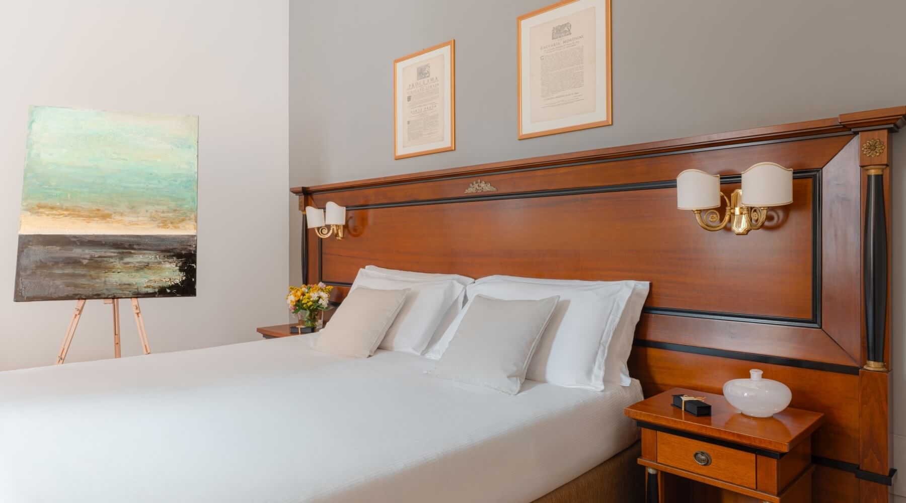 Camera da letto serena con letto grande, testiera in legno scuro, biancheria bianca e fiori in un vaso.