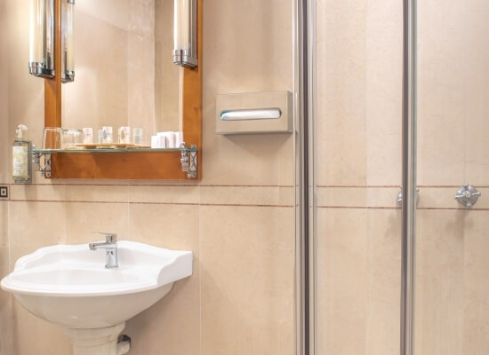 Immagine di un bagno compatto con lavabo, specchio, doccia parzialmente visibile e tonalità beige e pesca.