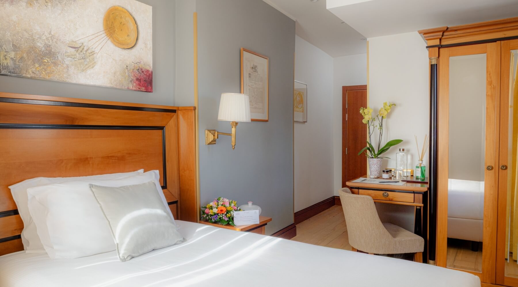 Camera da letto con letto, scrivania e armadio, decorata con fiori, lampada e opere d'arte, illuminata da luce naturale.