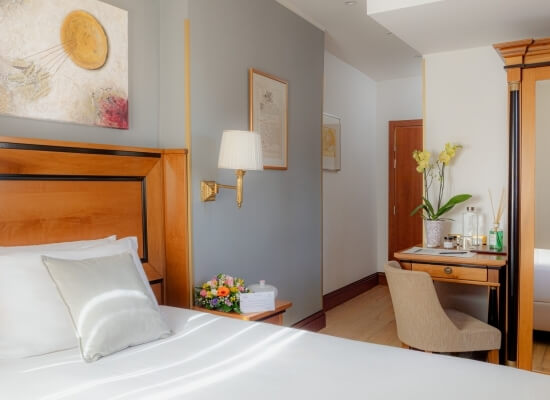 Camera d'hotel elegante con letto matrimoniale, decorazioni floreali, vanity e tonalità grigie che trasmettono tranquillità.