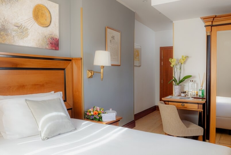 Camera da letto elegante e serena con un letto bianco, pittura astratta, comodino e scrivania, creando un'atmosfera rilassante.