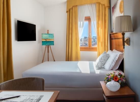 Camera da letto moderna con letto bianco, comodino, TV, cassettiera, sedia, cavalletto e decorazioni artistiche.