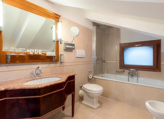 Elegant bathroom under a pitched roof with dark wood vanity, cream countertop, and sleek bathtub, featuring stylish decor.