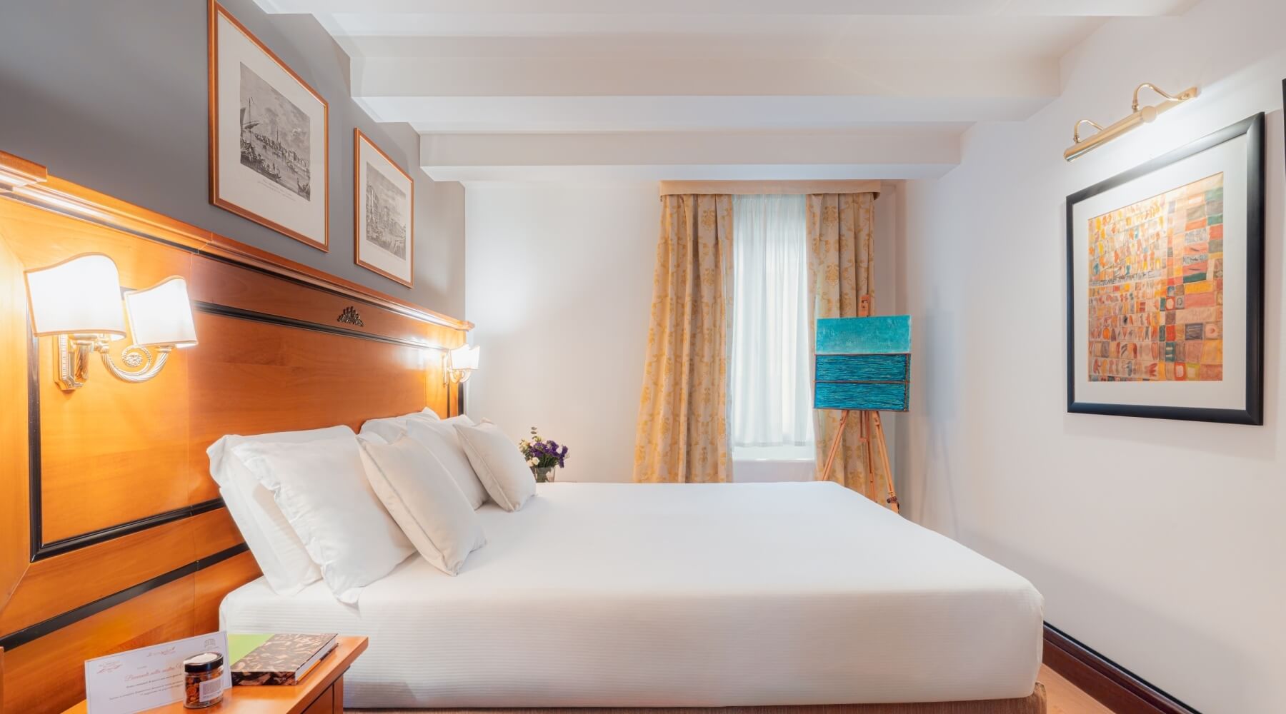 Camera d'hotel elegante e serena, con letto bianco, opere d'arte vivaci e dettagli raffinati in un'atmosfera accogliente.