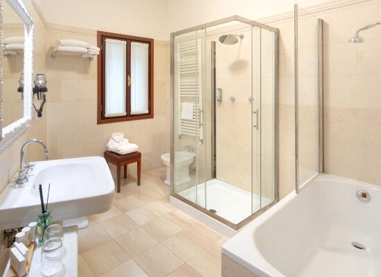 Bagno ben curato con doccia in vetro, vasca bianca, lavabo, specchio rettangolare e finestra con telaio marrone.