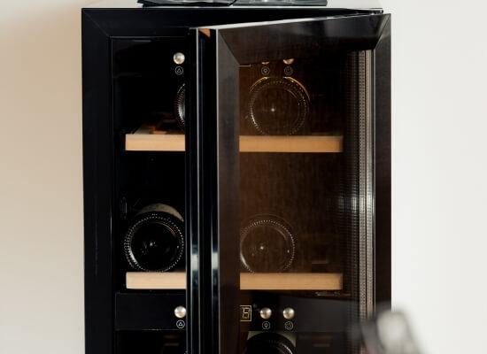 Frigorifero per vino nero con due porte in vetro, manopole argentate e ripiani in legno chiaro, su sfondo bianco.