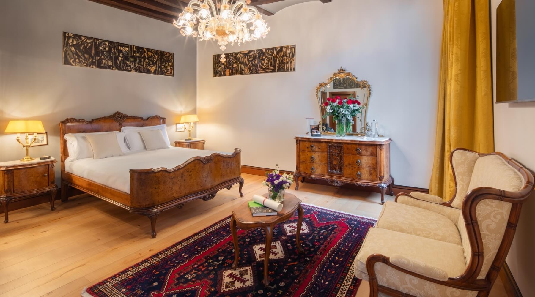 Camera da letto tradizionale con letto in legno scuro, comodini, cassettiera, specchio, sedia e tappeto colorato.