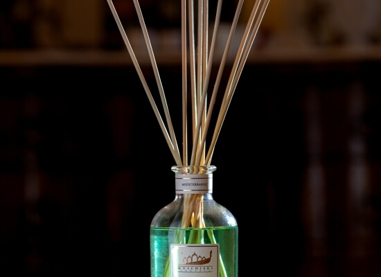 Bottiglia di vetro con liquido verde e bastoncini di legno, etichetta "MUCHITA" su sfondo scuro e sfocato.