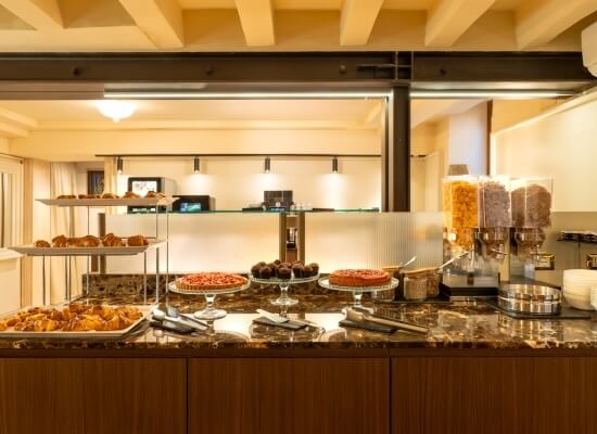 Buffet ben organizzato su un piano in marmo, con dolci, frutta e utensili da servizio.