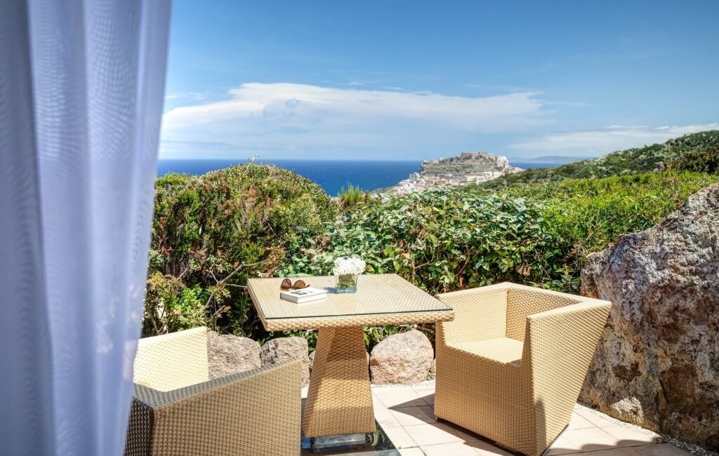 Ein ruhiger Patioszene mit einem Tisch, zwei Stühlen, Blumen, einem Buch und einer Aussicht auf eine grüne Landschaft.